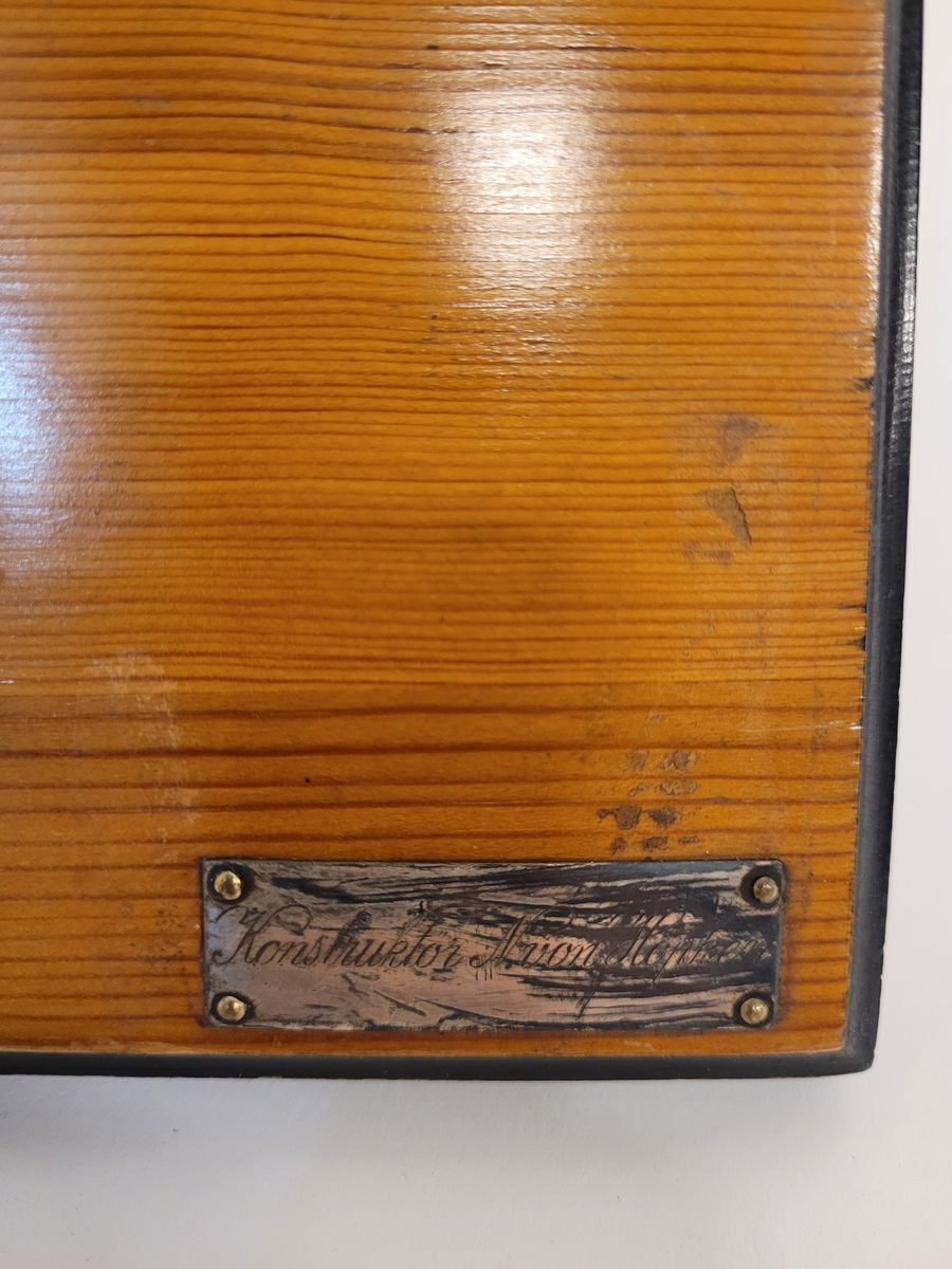 Halvmodell av yawlen Arla, i block av trä, visanda styrbords sida. Skrovet är svar och brunt, polerat. Monterat på polerad ljus träplatta med svart kant. Två silverplåtar med graverad text.