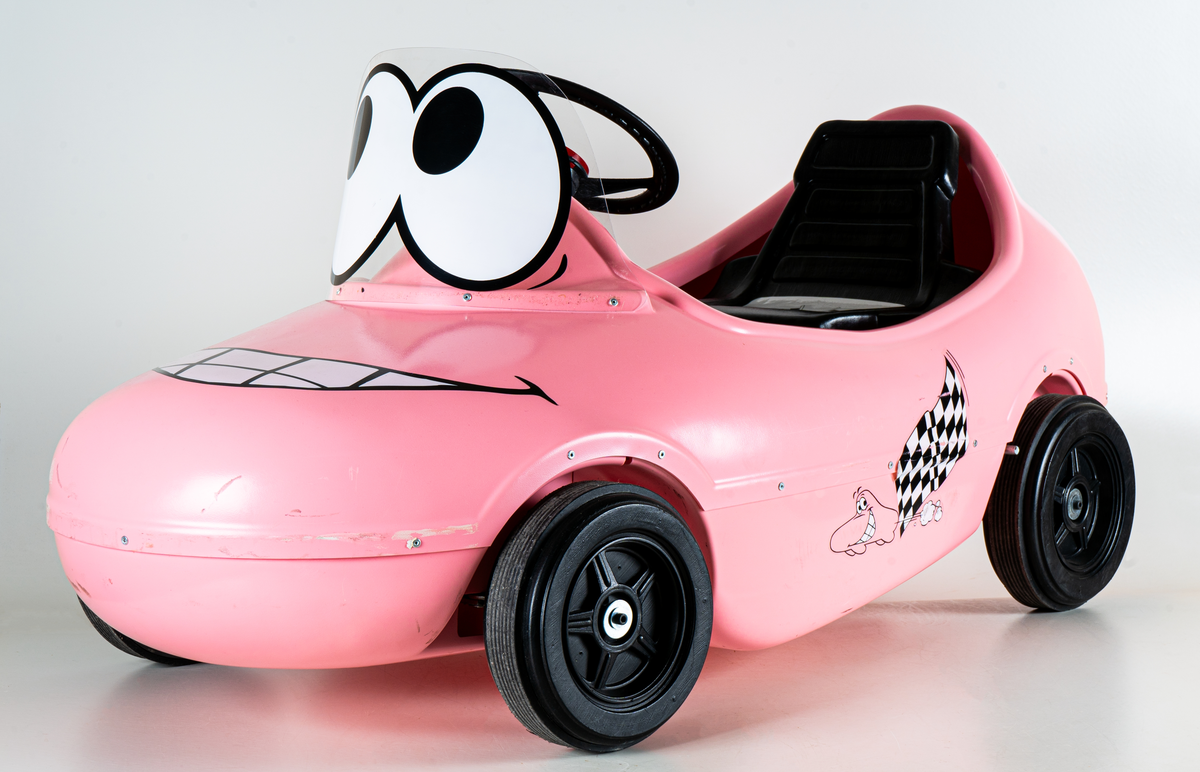 Trampbil av rosa plast, i form av en Ahlgrens bil. Fyra svarta hjul, svart ratt, dekaler på utsidan.