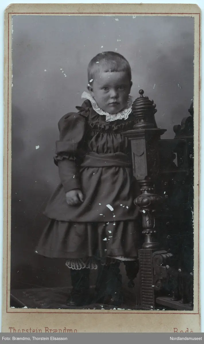 Portrettbilde av en liten jente i kjole. Gerda Marie Fremmerlid. Helfigur. Atelierbilde.