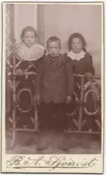 Gruppeportrett av tre barn foran og bak et smykkegjerde lage