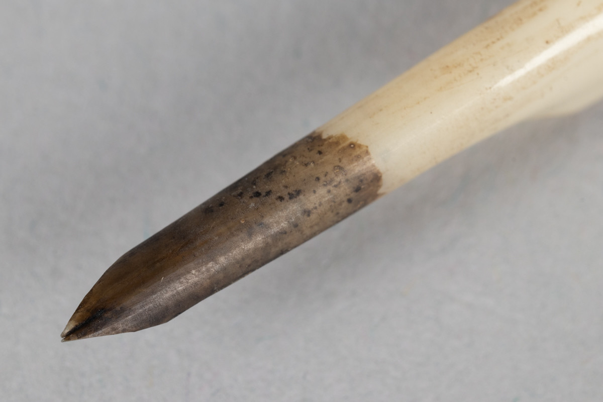 Velbrukt grå fjærpenn med blekkrester i tuppen. Mye av fjæra er skåret bekk