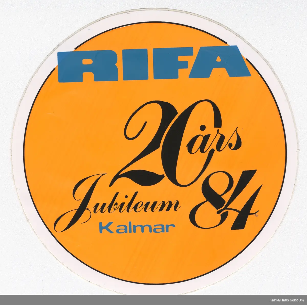 KLM 46772:3. Klistermärke. Runt klistermärke med färgtryck. Orange botten, vit ram, text i blått och svart. Text: Rifa 20 års Jubileum 84 Kalmar.