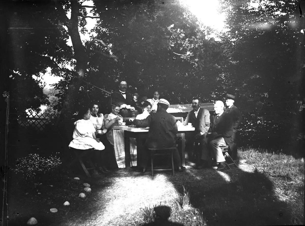 "Vid kaffebordet på Sätra den 2 juni 1899."
Bilden är troligen tagen av Axel Pehrson som hade sommarställe på Sätra; Sjöstugan nere vid bryggan.