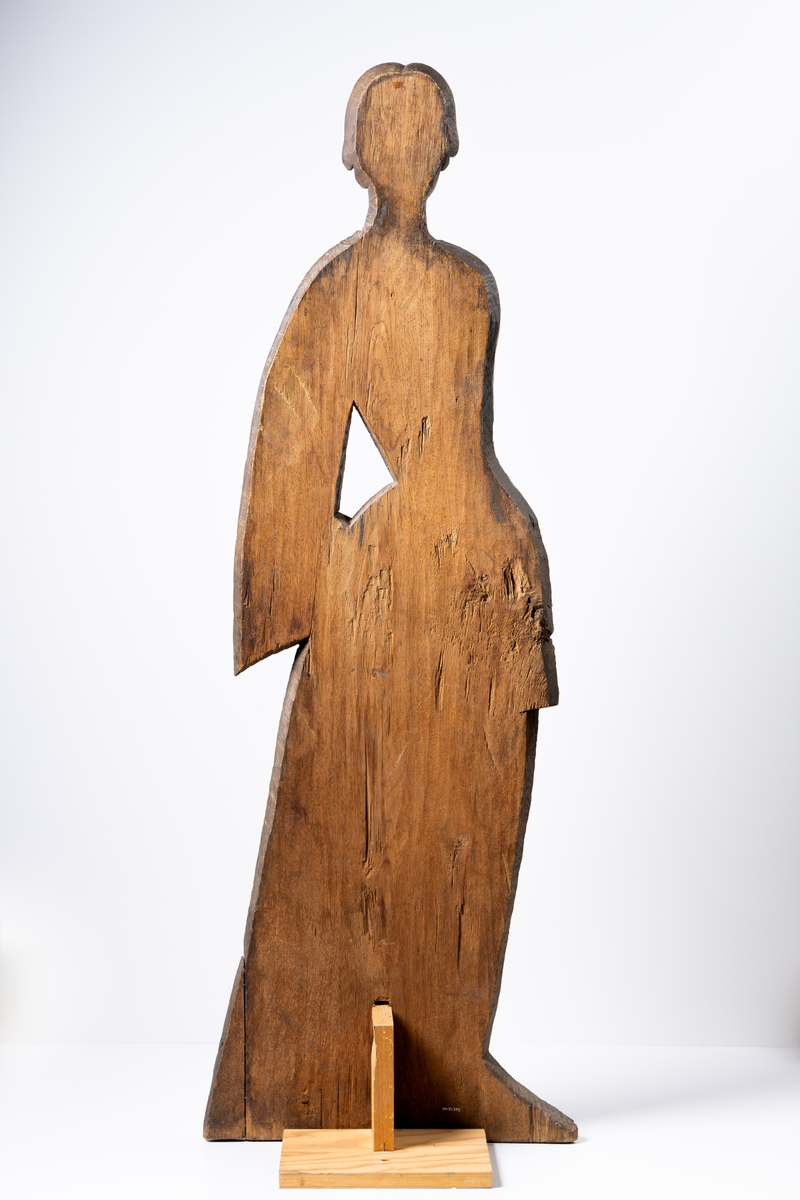 Parkfigur/trädgårdsfigur av trä. Figursågad och bemålad planka. Kvinnofigur iförd rödbrun klänning av 1700-talsmodell. I handen håller hon en solfjäder. Omålad baksida, nygjort stöd.