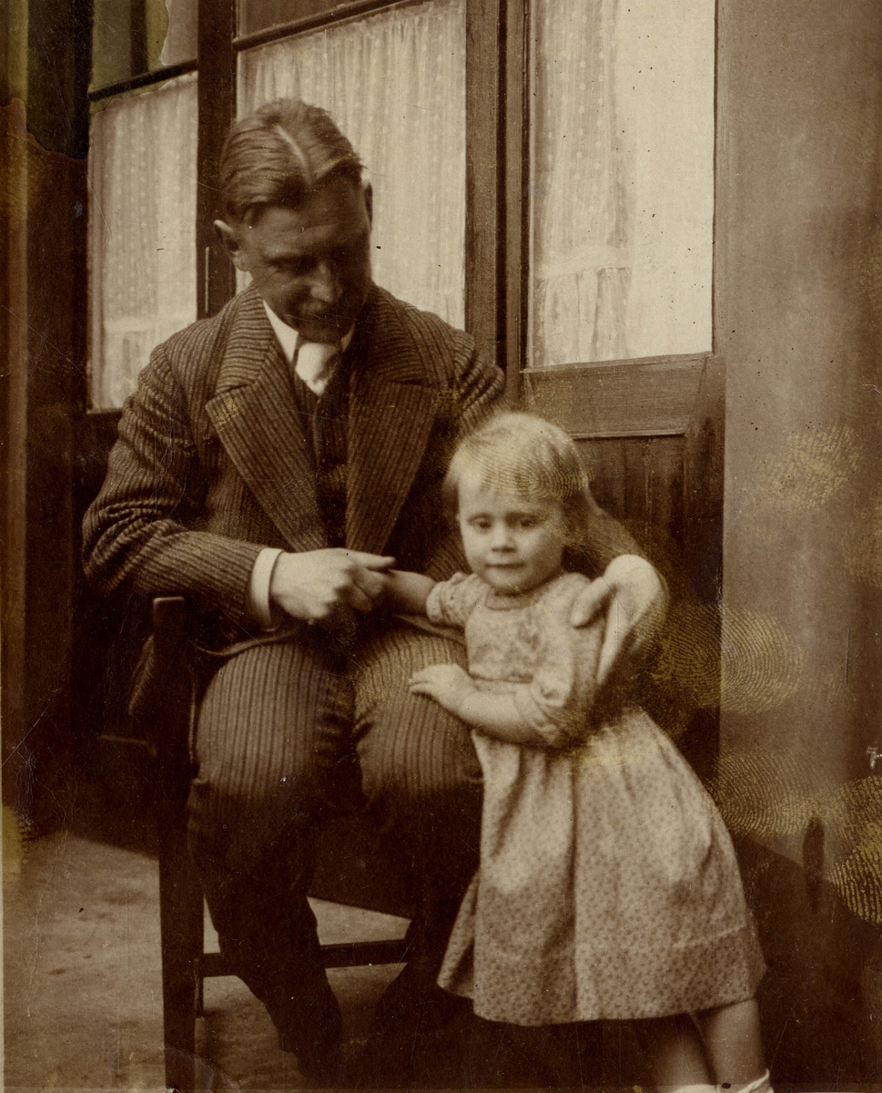 Mann sittende i stol, og liten jente foran vindu.