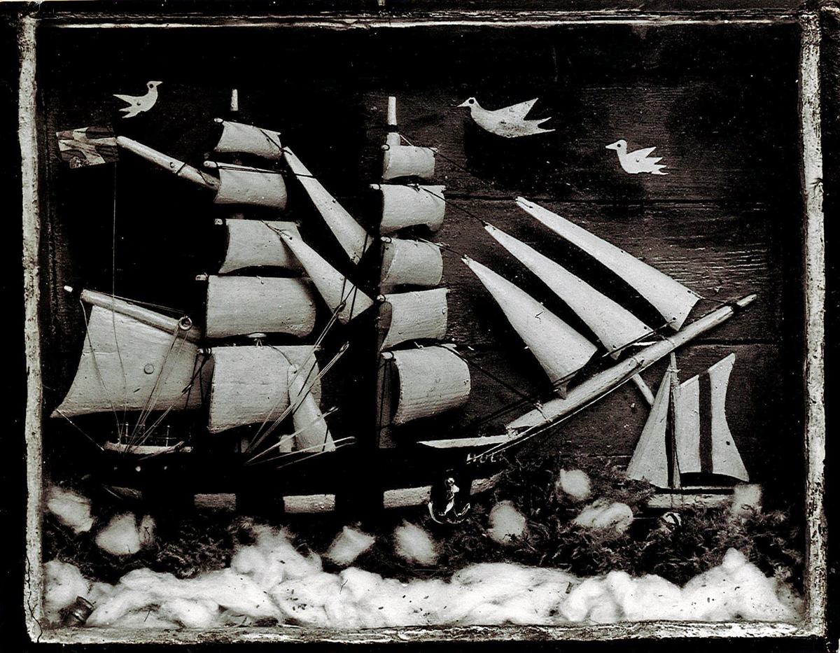Fartygsmodell i tavellåda, föreställande briggen HULDA. Halv i block av trä, visande styrbords sida. Riggad med segel av trä. Svart sida med grön rand och vit portmålning. Under gaffeln svensk flagg. Tavellåda av trä och glas.