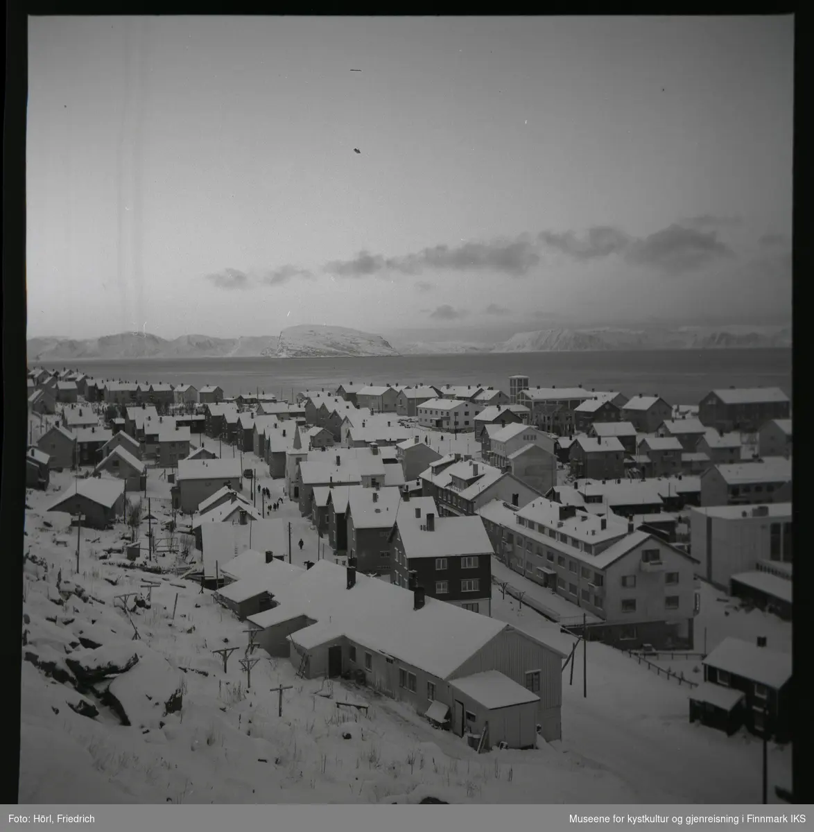 Utsikt over bydelen Hauen i Hammerfest i vinteren 1957/1958. Bildet er tatt fra Salenfjellet i retning Håja i Sørøysundet. De fleste bygninger er gjenreist. Markant er brannstasjonen med tårnet.