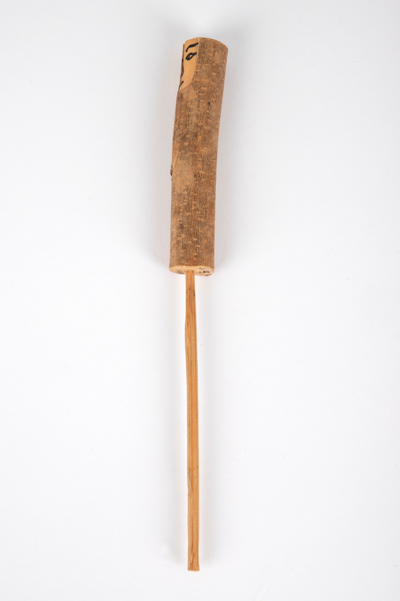 Tredukke laget av en trepinne med bark montert på en tynn pinne. Ansikt av ubehandlet tre, malt med svart. Dukken forestiller en mann og hører sammen med NK1991-039-003 (kvinne).