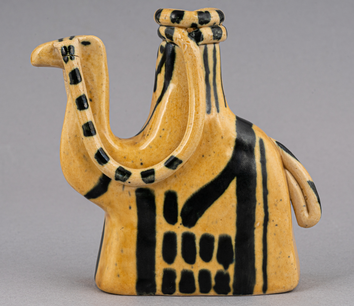 Figurin i lergods, kan även användas som ljusstake för julgransljus. Modell 6001, formgiven av Eva Jancke Björk under 1940- eller 1950-talet. Glasyr/dekor SV; curryfärgad bottenglasyr med svart dekor. Figurinen föreställer en arab sittandes på en kamel.