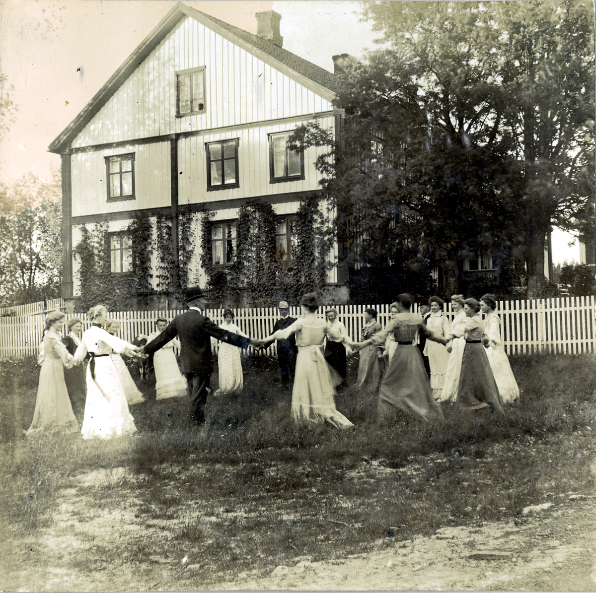 Kvinner og menn danser ute, på torvet 1904.
Bilde er fra fotoalbum GM.036887.