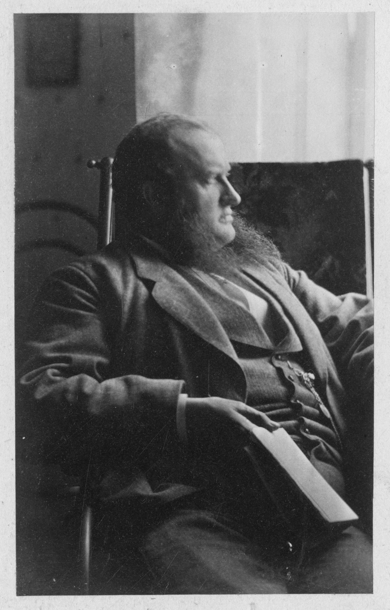 Foto av Henrik Moestue sittende i stol med en bok i hånden. Trolig tatt på 1870-tallet