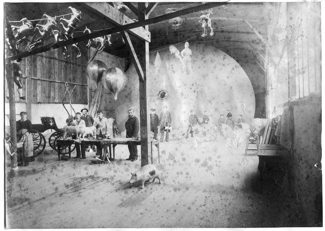 Interiör från en luftballongfabrik: "Ateliers Aérostatiques de Vaugirard" tillhörande Henri Lachambre. Kvinnor vid symaskiner i bakgrunden framför en fylld luftballong. Mindre reklamballonger i förgruden i form av bland annat olika djur.