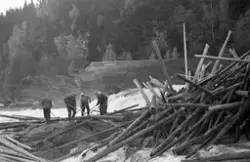 Fem fløtere i arbeid med å løsne tømmerhaugen som hadde bygd
