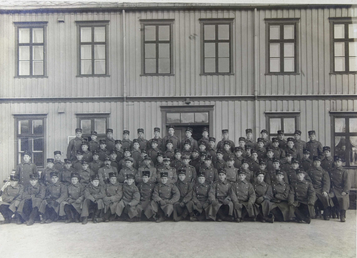 En gruppe soldater i vinteruniform oppstilt foran en trebygning.