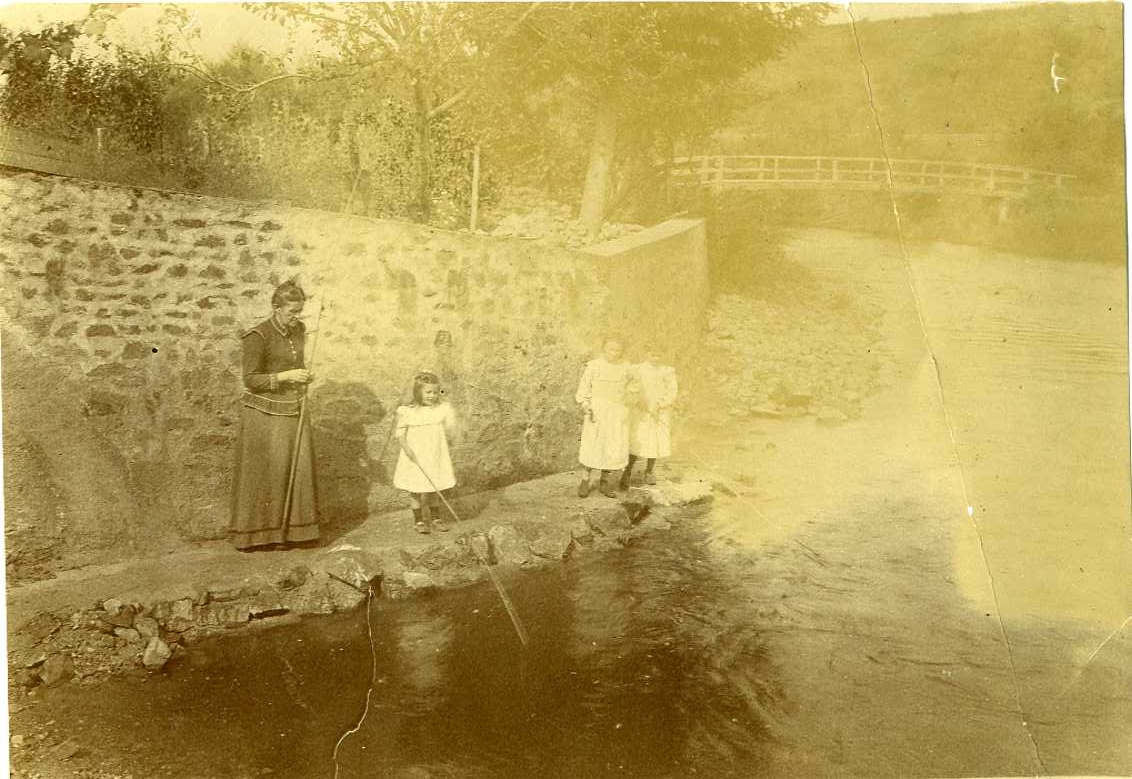 En kvinna och en liten flicka står vid ett vattendrag med varsitt metspö. Det är Céline Machuron och barnbarnet Marcelle Machuron. En bit ifrån dem står två andra flickor, också de med metspö