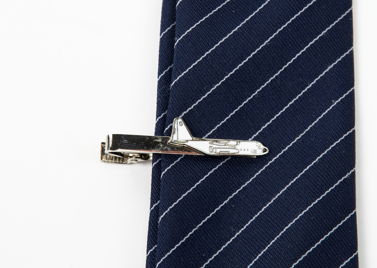 Blå slips med smala vita diagonala ränder och en bild på flygplan Tp 84. Till slipsen hör en slipsnål även där med en bild på flygplan Tp 84.
