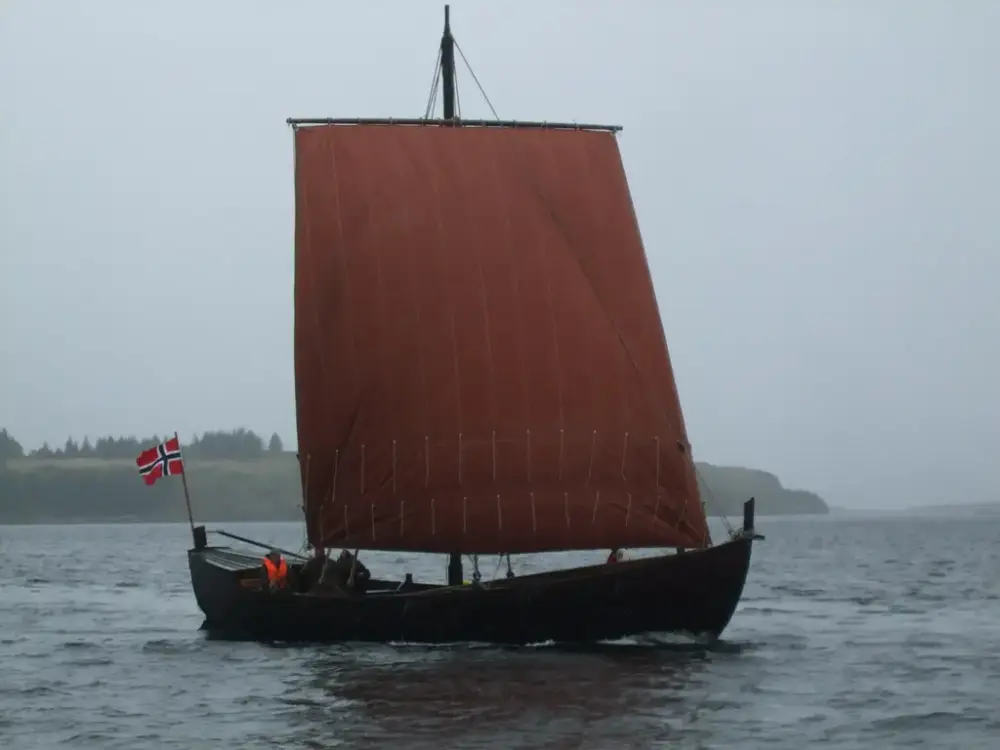 Skuta ute i fjorden. Skuta er i tre med et stort rødt segl.