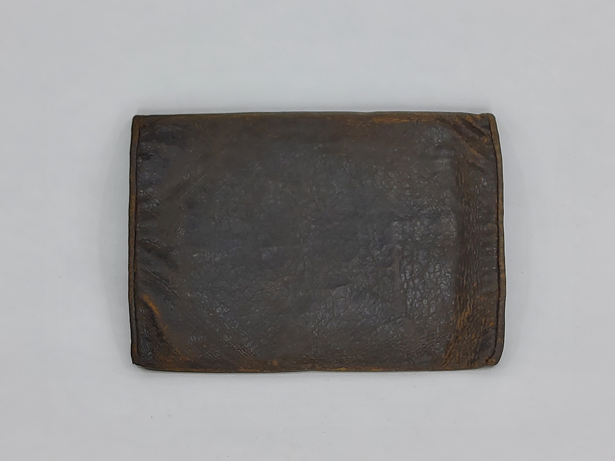 Plånbok av svart läder med flera fack. Ett fack innehåller brev med upplysningar. Tillverkad av givarens morfar 1860.