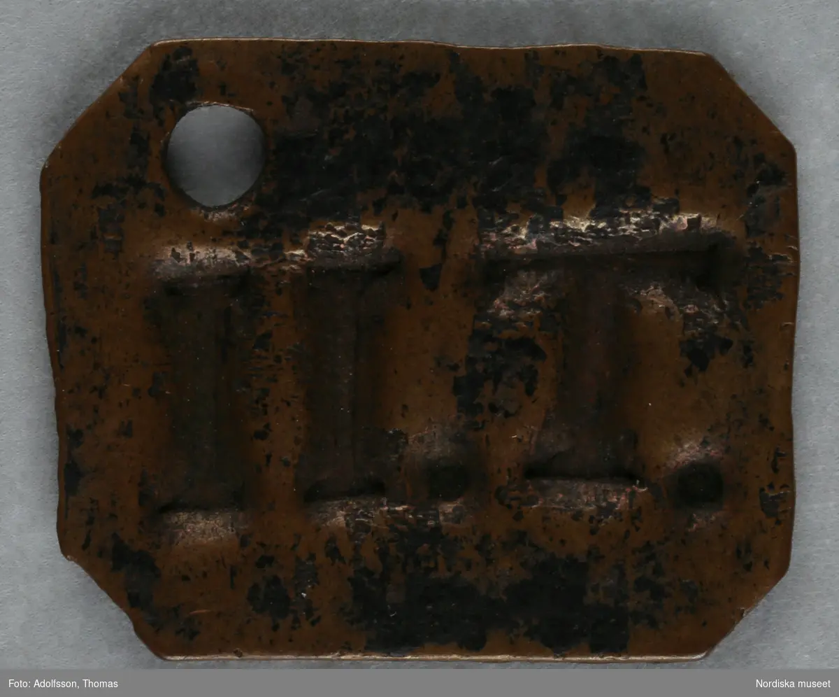 Pollett av koppar, åttakantig (rektangel med avklippta hörn); inslaget hål, stämplat: II. T.