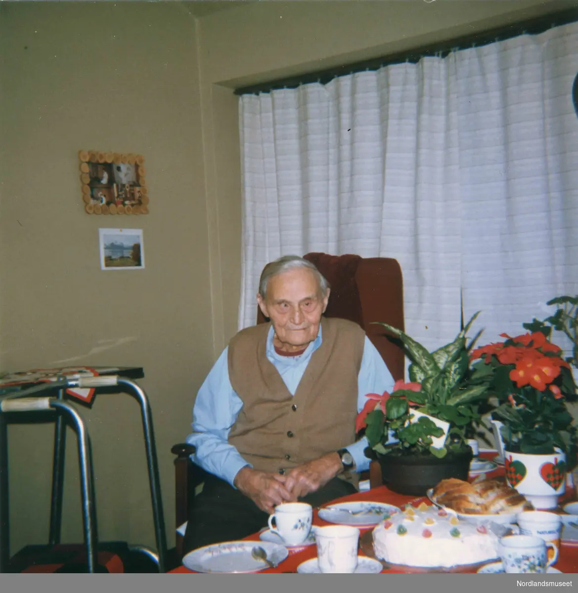 En eldre mann sitter i en stol. På bordet ved siden av er det kake, kaffeservice og potteplanter. Ingvar Størdal, bror til Klara Simonsen, Bodø.