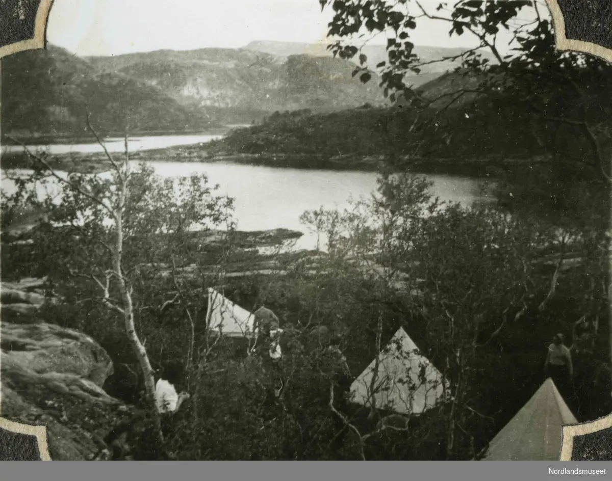 Et landskap med fjell og innsjø. I forgrunnen ser vi oppslåtte telt og mennesker. Bildetekst: "Leiren ved Valnesvatnet. Høsten 1943".