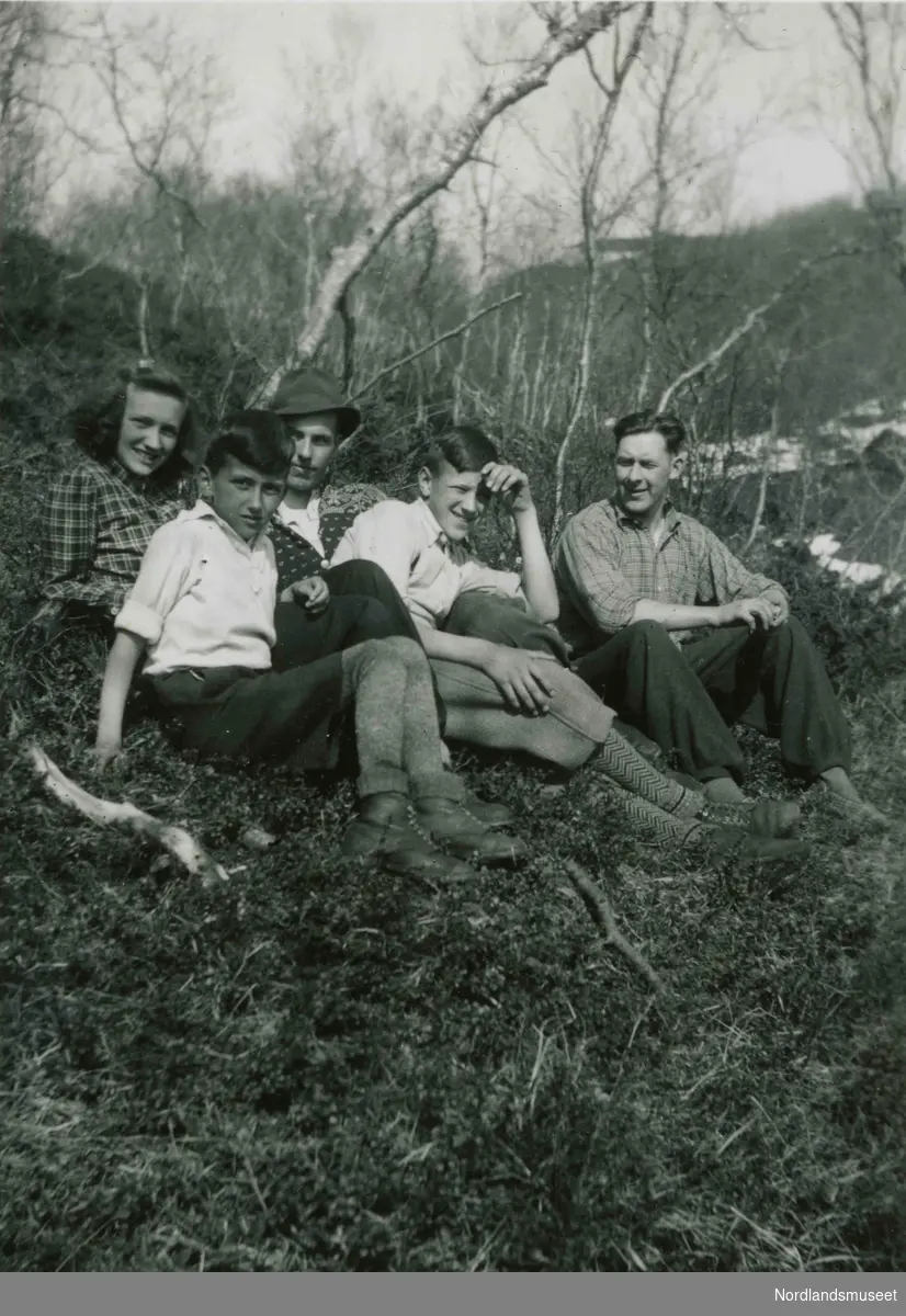 Fem unge personer ligger i gresset. Den ene har på seg strikkejakke.