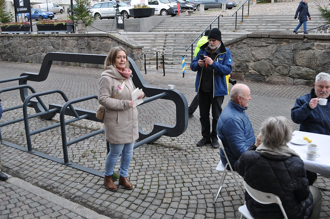Folk sitter vid dukat bord på Brahegatan utanför kafé Fiket i Gränna. En kvinna håller ett tal, en man filmar henne.