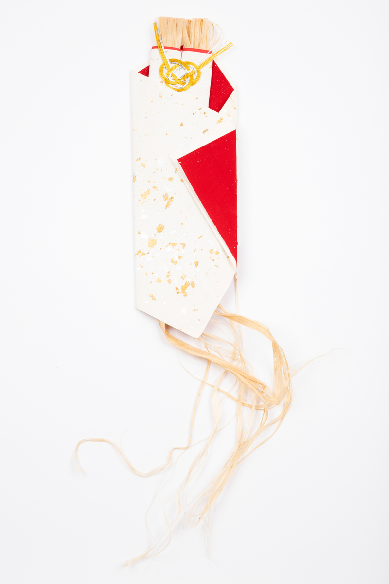 Pakke brettet av ubleket tykt papir med gull- og sølvfargede "flekker". Innvendig fór av rødt papir med sølvprikker. Pakken er kunstferdig brettet og har strå inni, som er et symbol for tang.