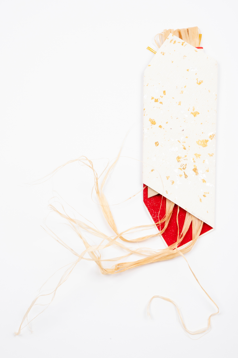 Pakke brettet av ubleket tykt papir med gull- og sølvfargede "flekker". Innvendig fór av rødt papir med sølvprikker. Pakken er kunstferdig brettet og har strå inni, som er et symbol for tang.