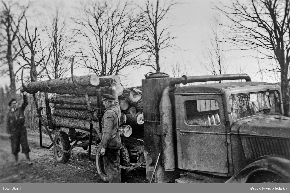 Tømmerlessing på bil med vedgassgenerator ved Utne i Rygge ca. 1944. Fremst: Gunnar Rødsrud, eier av bilen.
Lastebilen er en Ford V8 1936-modell med norskbygd førerhus.