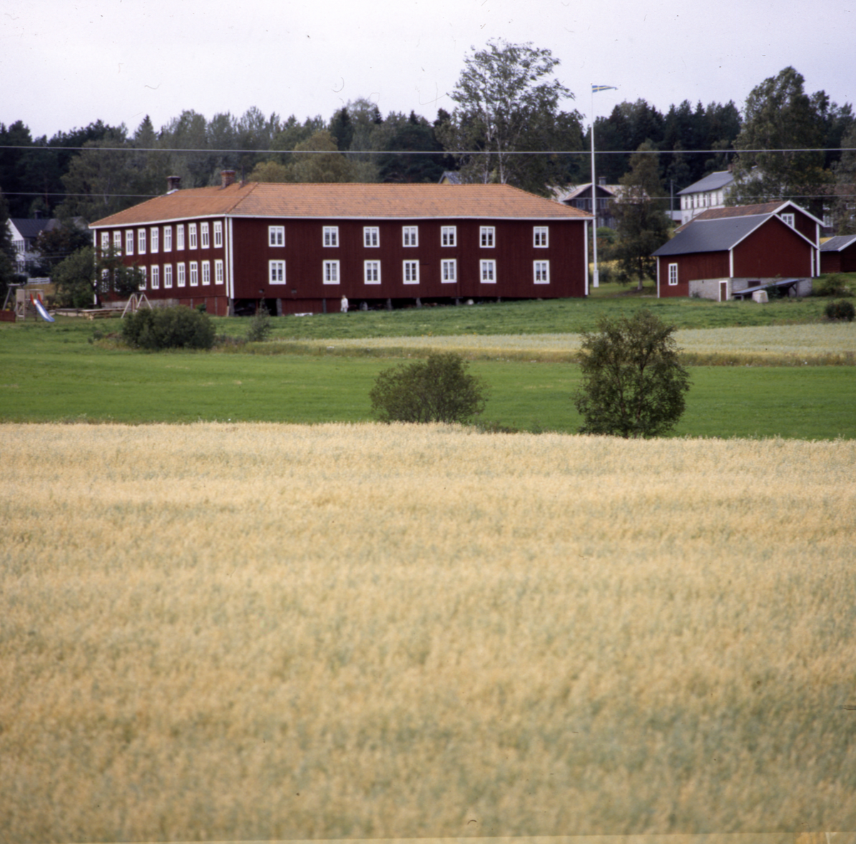 En gård med ett stort hus samt några mindre hus och åkermark.