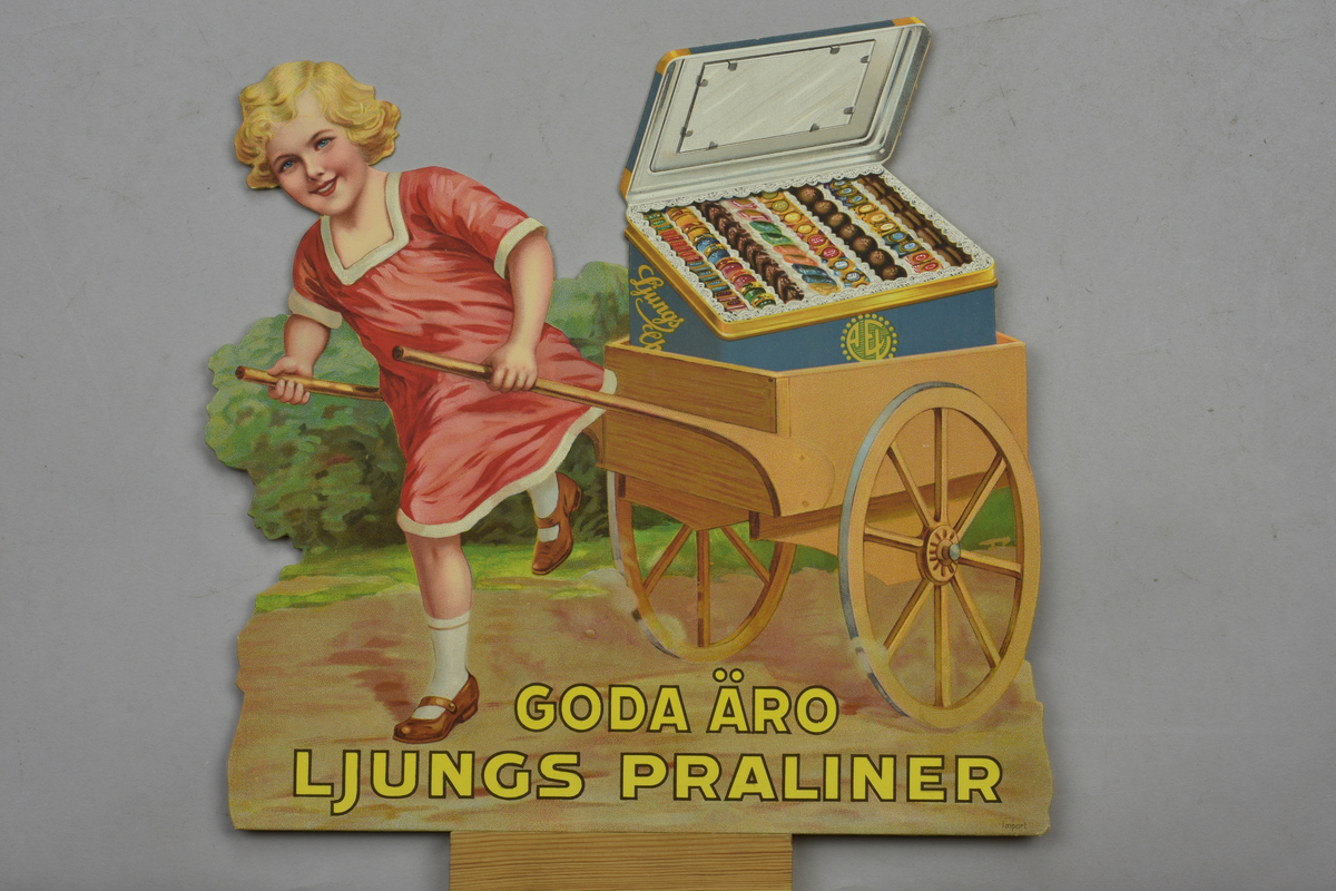 Reklamskylt visande flicka som drar kärra med en låda praliner. Text: "Goda äro Ljungs praliner". För Ljungs Chokladfabrik.