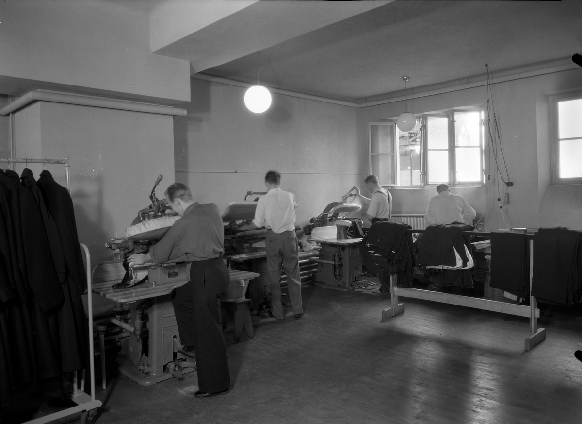 A-B. Bergsson och söner; interiör av fabriken. Män i arbete vid pressmaskiner.
Företaget som var känt över hela vårt land som ett av de större i konfektionsbranschen och grundades 1900 av framlidne grosshandlaren B.Bergsson och hans två äldsta söner som grosshandelsfirma i manufakturbranschen. 1914 upptogs egen tillverkning av herrkläder. 1929 skedde en första tillbyggand av fabrikslokalerna. Åren 1935-36 utökades fabrikslokalerna till det dubbla och företaget har kunnat glädja sig åt ett fullt utnyttjande av sin kapacitet c:a 40.000 plagg per år. Firman hade även upptagit tillverkning av damkappor och damdräkter.
Källa: Nyblom-Svanqvist, Näringsliv i Värmland.1945.