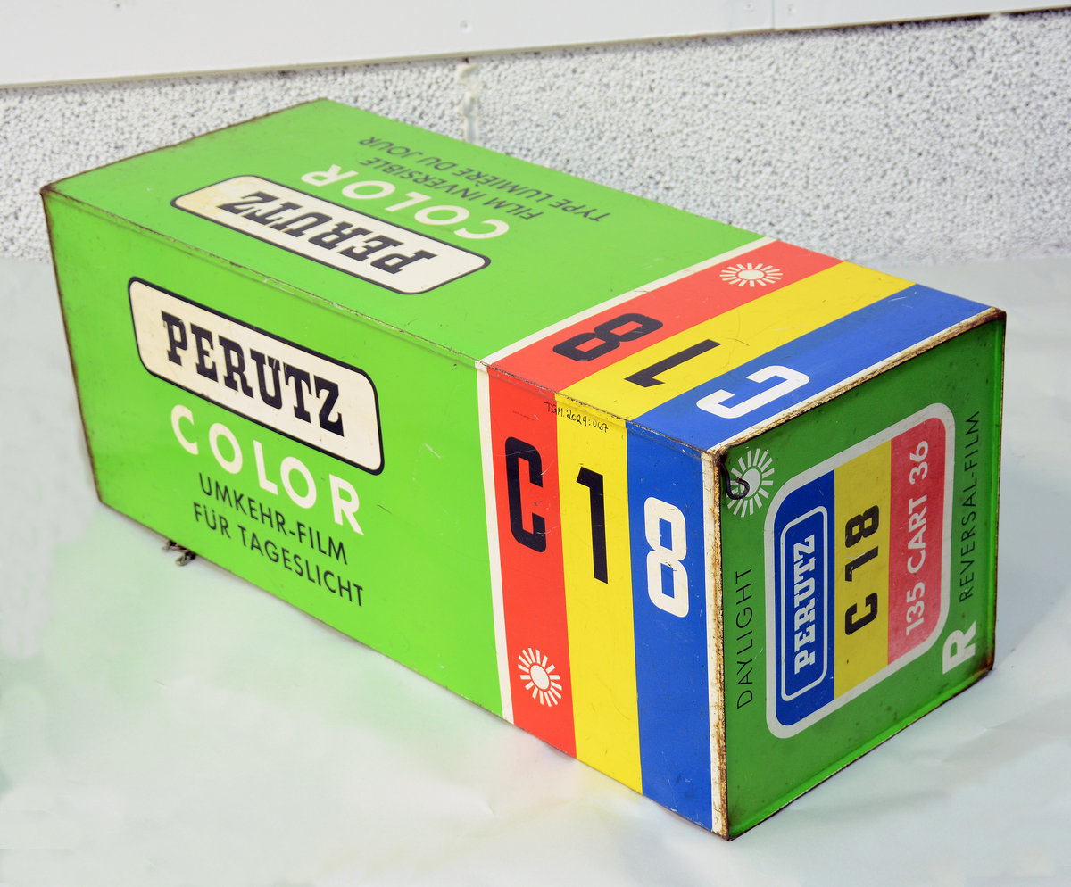 Reklame for Perutz Color C18, formet som en stor filmboks i metall med oppheng, til å henge opp på utsiden av fotobutikken.