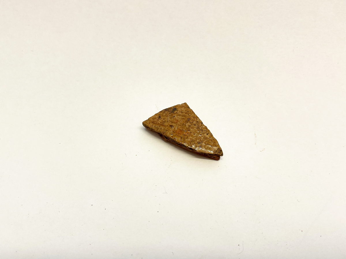 Ett bukfragment av (äldre?) rödgods med senapsgul glasyr på utsidan. Oglaserad insida. Drejlinjer. Möjligen del av en kanna eller gryta. Mycket lik M 48845-38a, 42 och 43.