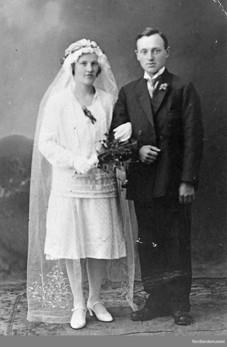 Portrett av brudeparet Judith og Helge Gundersen. Bruden har kort hvit kjole, hvitt langt slør og hvite sko.
