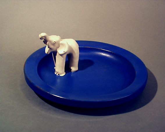 Runt askfat av lergods med halvmatt glasyr i blått, vid kanten  en vitglaserade modellerad elefant. Fatet gjutet. I botten stämplat: EKEBY 46.