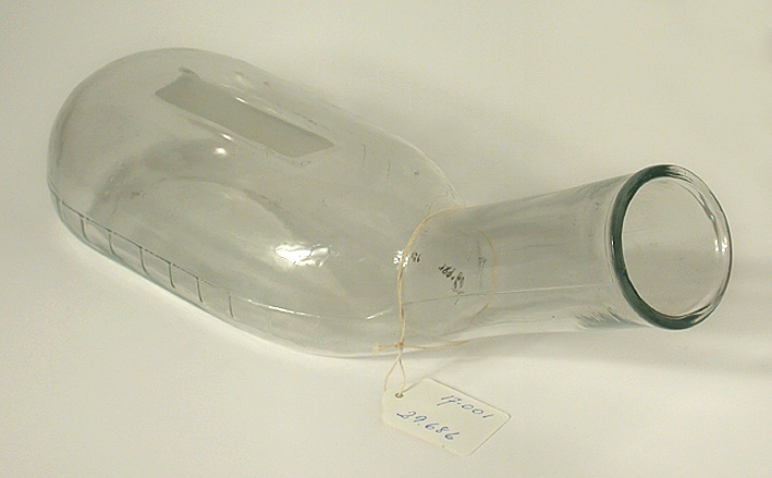 Bäcken i form av en liggande, platt flaska i ofärgat glas med snedställd hals. Graderad skala i relief på sidorna. 100-1000 millimeter. Etsad yta (ca 85x25 mm) på ovansidan.