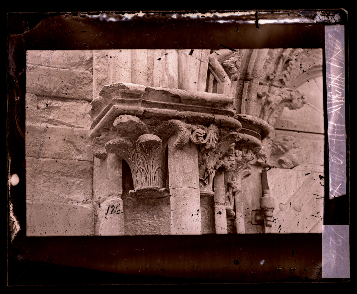 Kapitel i sør-østre portal i oktogonen i Nidarosdomen (Bispeinngangen). Kapitelet sitter på venstre side av døren. I bakgrunnen ser man en del av buen med krabber. Bildet er tatt før restaurering.