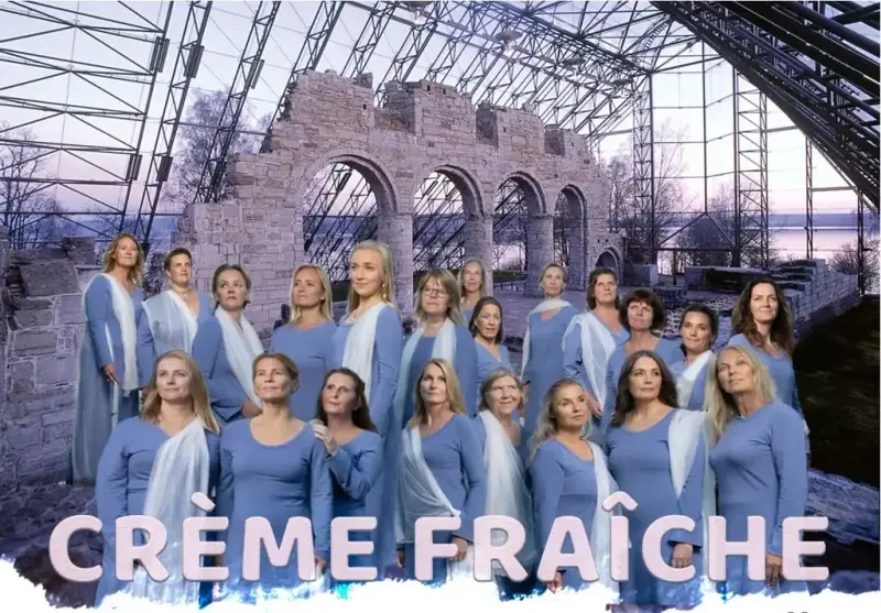 Damekoret Crème Fraîche står i duse, blå korkjoler med domkirkeruinen i bakgrunnen.