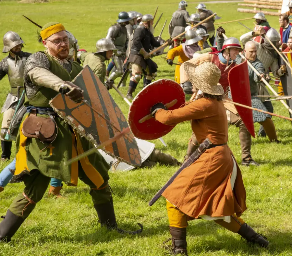 To krigere i middelalderantrekk med skjold og sverd som sloss mot hverandre