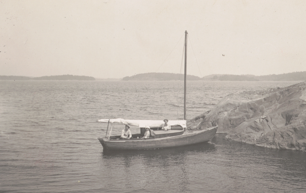 Två kvinnor och man i segelbåt vid klippa i Stockholms skärgård.