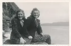 To kvinner sitter sammen på en stein i fjæren foran havet ut
