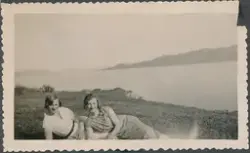 To kvinner ligger i gress landskap, de lener seg på hverandr