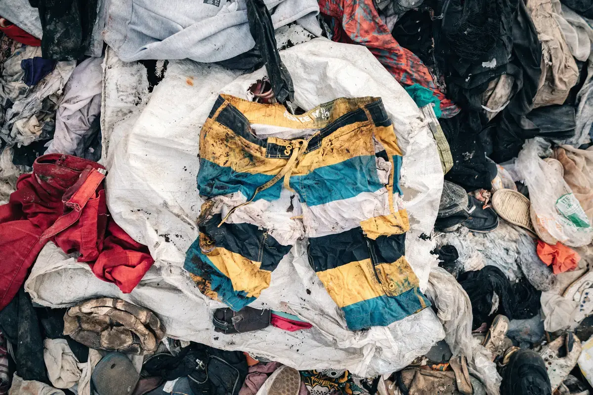 Bildet viser moteklær liggende på en søppelfylling, i semtrum i bildet ligger det en shorts som har striper i fargene svart, gul, blå og hvit.