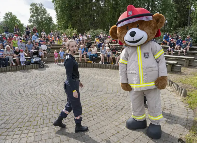 Brannbamsen Bjørnis og en brannkvinne står foran en rekke mennesker i amfiet 