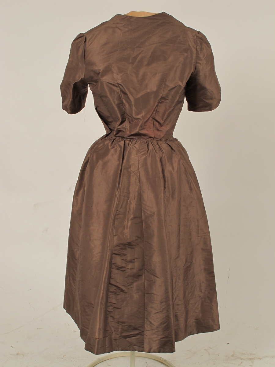 Omsydd kjole fra krigen 1940- 45,  Silketaft. mellombrun, med påsydde bånd i dypere brunfarge i ripsvevd silkemoiré.  

Opprinelig gallakjole slutten av 1880 årene, muligens 1888. Nå delt i opprinnelig overdel og løse deler.