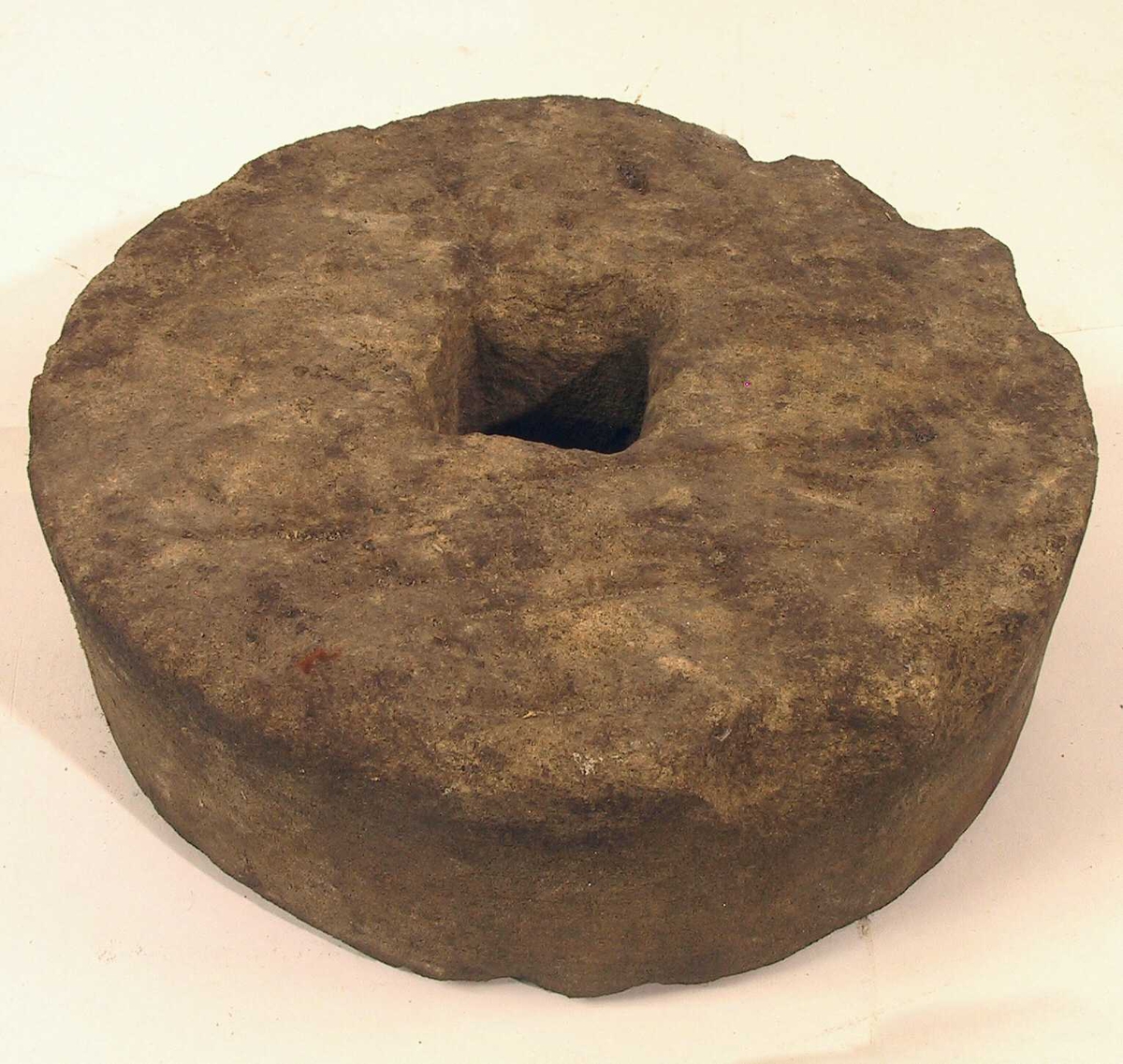 Rund sten med flat over- og underside og et firkantet hull i midten.
