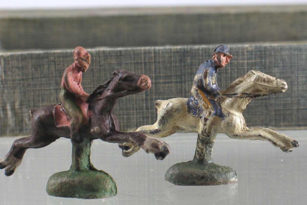 På esken: Hester med ryttere ved hinder, tribuner i bakgrunnen.