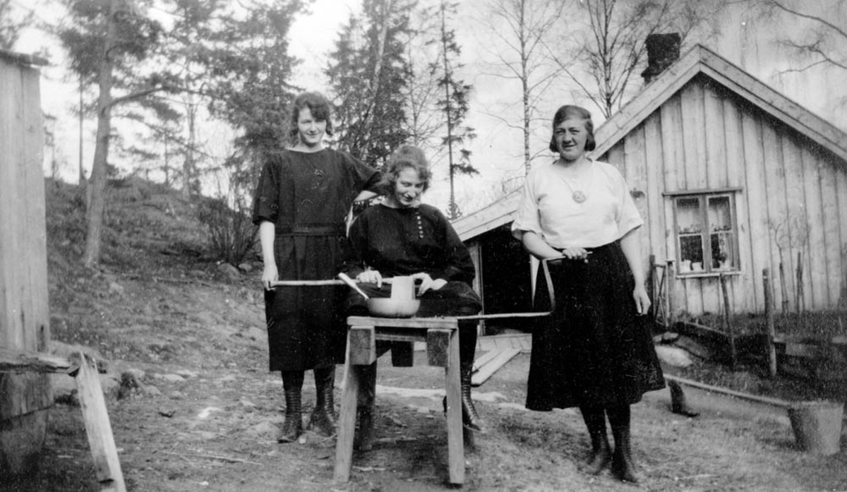 Inga, Helga og Marie Sørlie ved slipesteinen.  Sørlihuset bak.